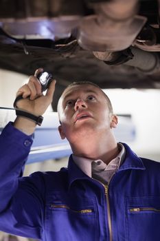 Mechanic holding a flashlight while looking at a car in a garage