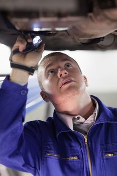 Mechanic illuminating the below of a car with a flashlight in a garage