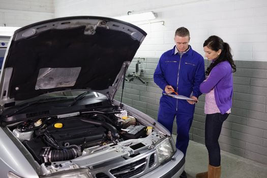 Mechanic holding a clipboard next to a woman in a garage