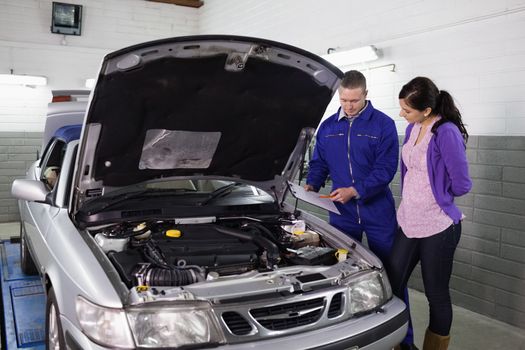 Mechanic showing a clipboard to a woman in a garage