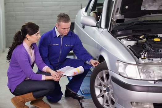 Mechanic showing the car wheel to a client in a garage