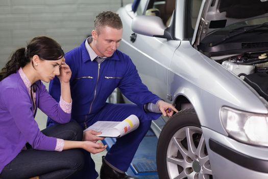 Mechanic looking at the car wheel next to a client in a garage