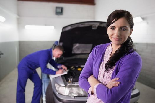 Woman with arms crossed next to a car in a garage