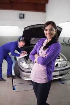 Woman smiling with arms crossed next to a car in a garage