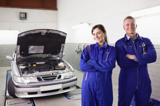 Smiling mechanics with arms crossed next to a car in a garage