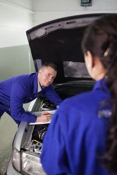 Mechanic leaning on a car while looking at a colleague in a garage