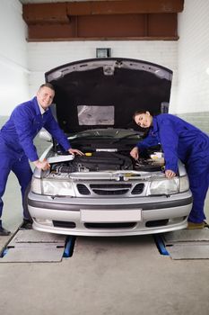 Mechanics smiling while leaning on a car in a garage