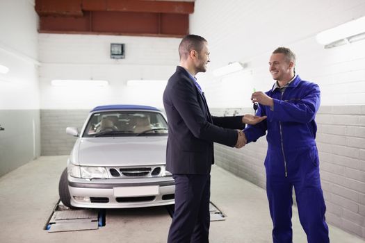 Mechanic giving car key while shaking hand to a client in a garage