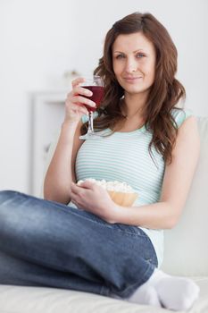 Woman holding a glass of red wine and a bowl of popcorn in a living room