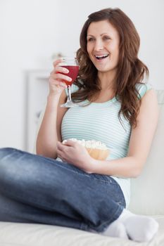 Woman holding a glass of wine and a bowl of popcorn in a living room