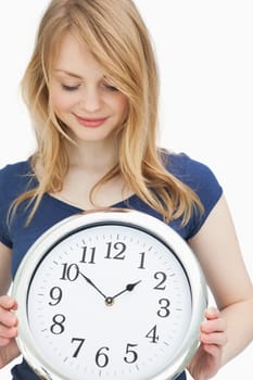 Blonde woman holding a clock while smiling against a white background