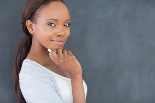 Black woman looking at camera while holding a chalk in a classroom