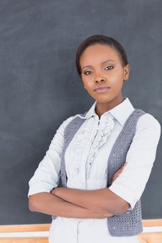 Serious teacher looking at camera with arms crossed in a classroom