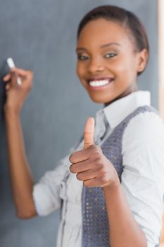 Teacher with thumb up writing on a blackboard in a classroom