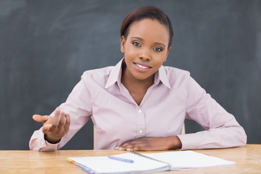 Teacher sitting at desk next to a notebook in a classroom