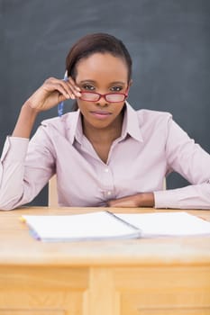 Teacher sitting at desk while touching her glasses in a classroom