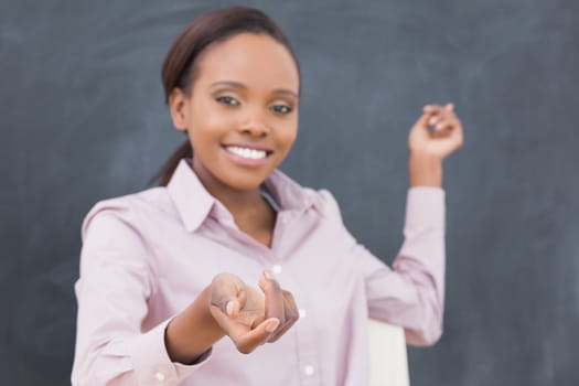 Black teacher showing the blackboard while smiling in a classroom