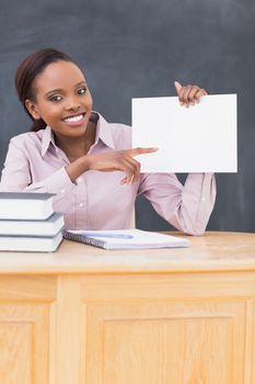 Black teacher holding a blank paper while sitting at desk in a classroom