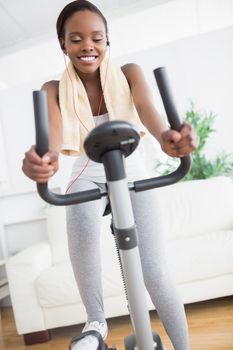 Black woman doing exercise bike while listening music in a living room