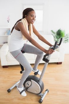 Black woman doing exercise bike while smiling in a living room