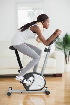 Side view of a concentrated black woman doing exercise bike in a living room