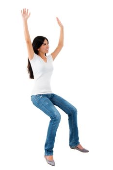 Excited young Asian girl raise her hands up, sitting on invisible chair over white background