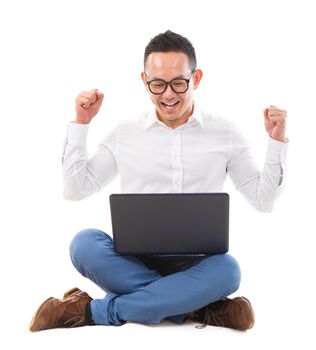 Excited Asian man using laptop on the floor over white background