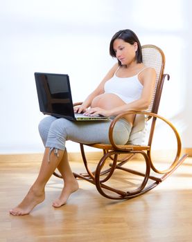 Beautiful pregnant woman at home with laptop computer on rocker chair