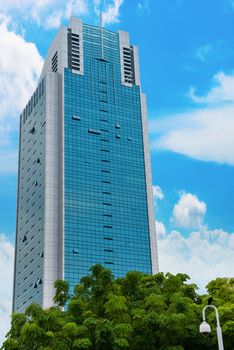 Skyscraper with blue sky on background and trees on front