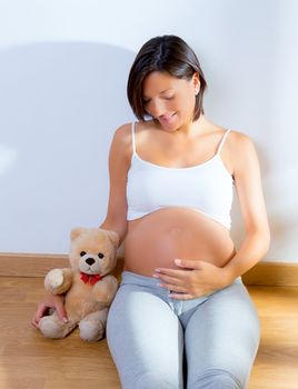 Beautiful pregnant woman sitting on floor with teddy bear