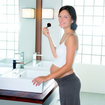 Beautiful pregnant woman on modern bathroom makeup with brush in mirror