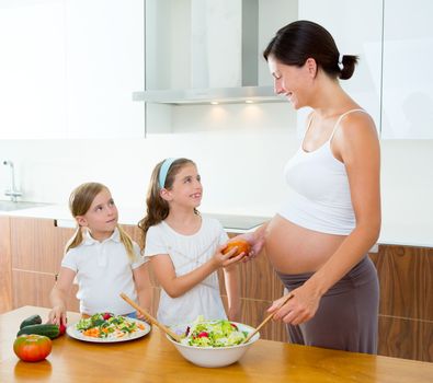 Beautiful pregnant mother with her daughters at kitchen preparing salad