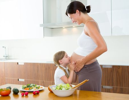 Beautiful pregnant mother with her daughter at kitchen kissing baby in belly