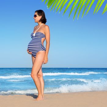 Beautiful pregnant woman standing on blue beach in summer vacation