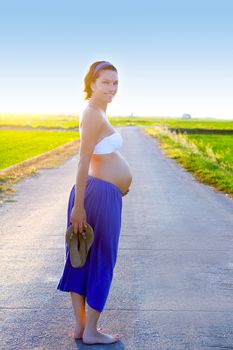 Beautiful pregnant woman walking on track at green rice fields