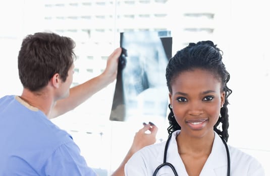 Doctor looking at a of X-ray while his colleague is posing in an office