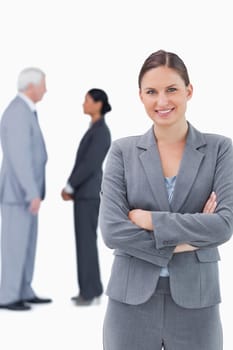 Smiling businesswoman with arms folded and colleagues behind her against a white background