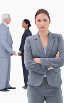 Serious businesswoman with folded arms and colleagues behind her against a white background