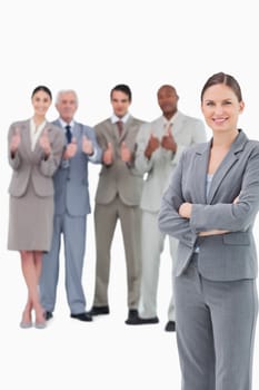 Smiling saleswoman with arms folded and her team behind her against a white background