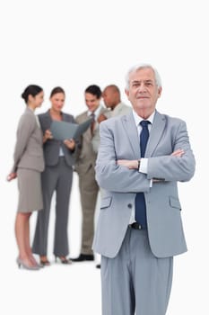 Mature businessman with arms folded and team behind him against a white background