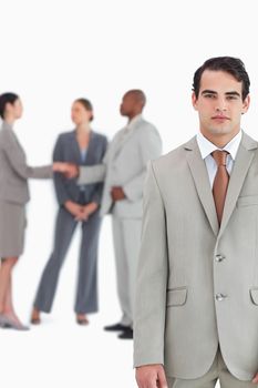 Serious salesman with businesspeople behind him against a white background