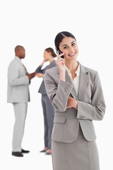 Smiling businesswoman with cellphone and colleagues behind her against a white background