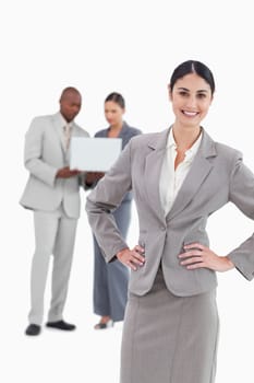 Smiling businesswoman with hands on her hip and colleagues behind her against a white background