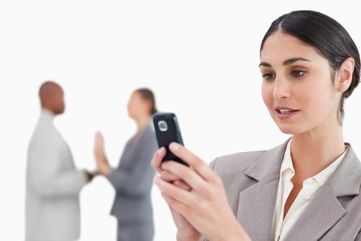Businesswoman looking at cellphone with colleagues behind her against a white background