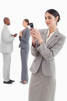 Businesswoman reading text message with colleagues behind her against a white background