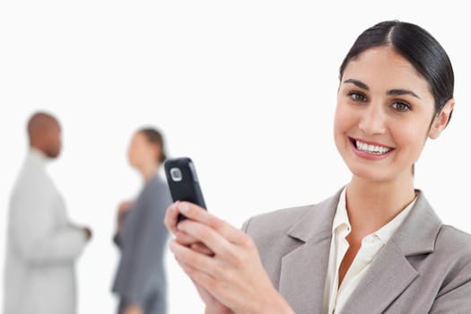 Smiling saleswoman holding cellphone with colleagues behind her against a white background