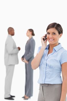 Smiling saleswoman on the phone with associates behind her against a white background