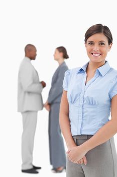 Smiling businesswoman with talking co-workers behind her against a white background