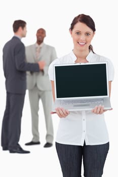 Businesswoman showing laptop with colleagues behind her against a white background