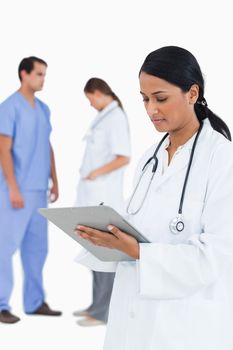 doctor taking notes with staff members behind her against a white background